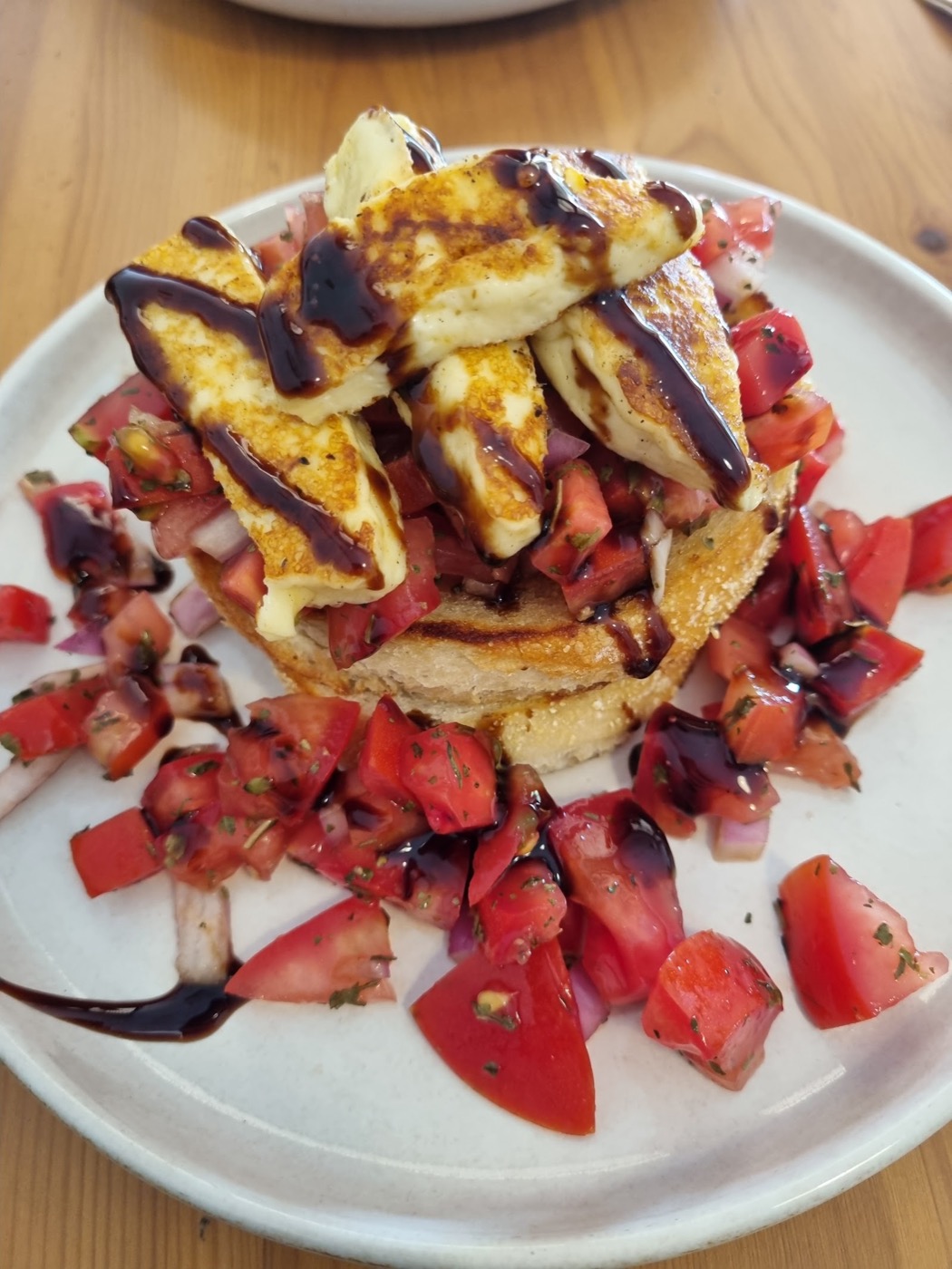 A plate of grilled halloumi slices on toast, drizzled with a dark glaze and surrounded by chopped fresh tomato